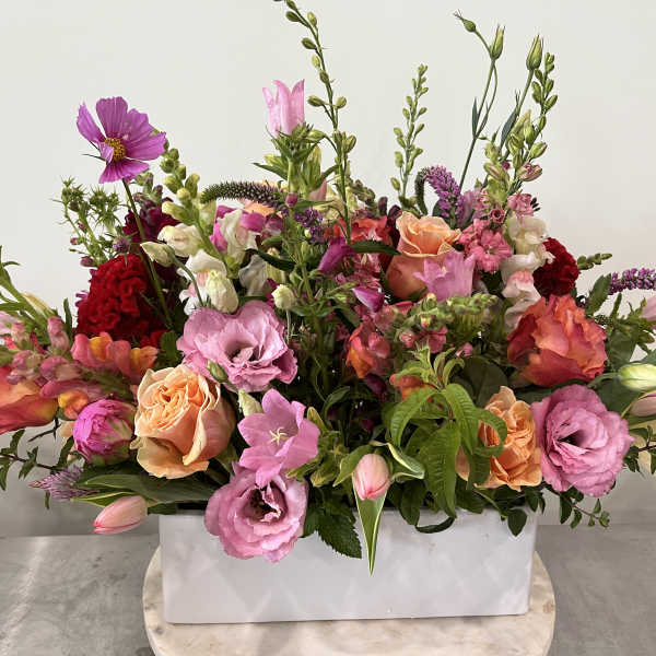 Large mixed bouquet in a white rectangular vase with pink, peach, and red blooms.