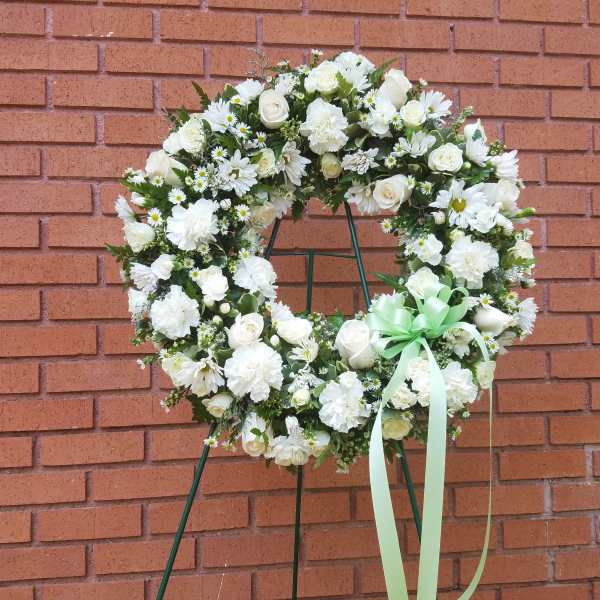 White floral wreath on a stand with a pale green ribbon