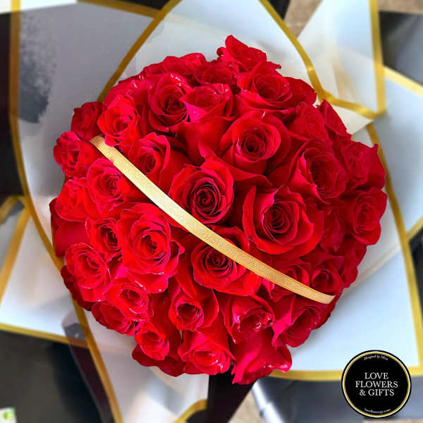 Round bouquet of tightly clustered red roses wrapped in white and black paper with gold accents.