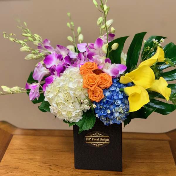 Colorful floral arrangement in a black box with orchids, hydrangeas, roses, and calla lilies