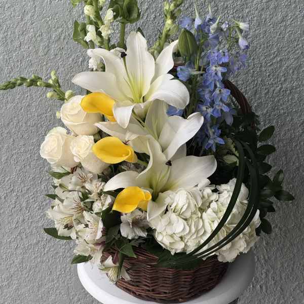 Basket arrangement with white lilies, yellow calla lilies, and blue delphinium