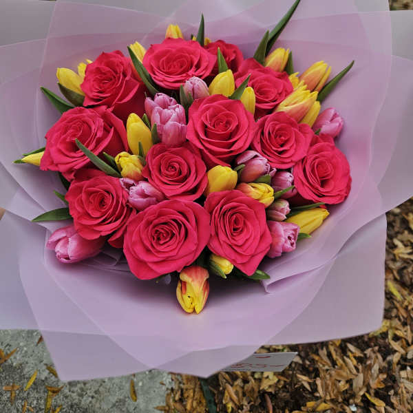 Bouquet of hot pink roses and yellow tulips wrapped in pale pink paper