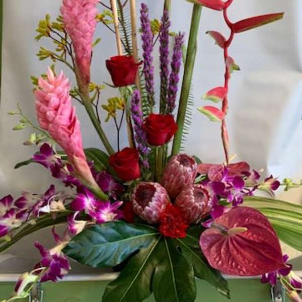 Tall tropical floral arrangement with pink and red blooms in a container