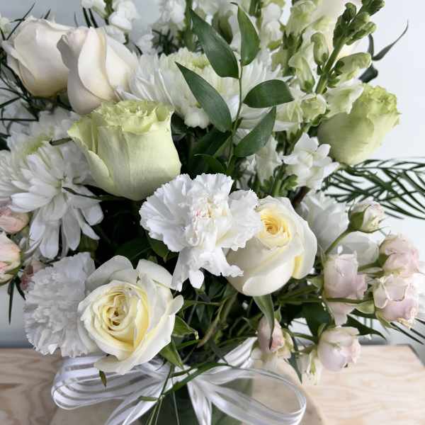 White roses and chrysanthemums in a glass vase with a ribbon