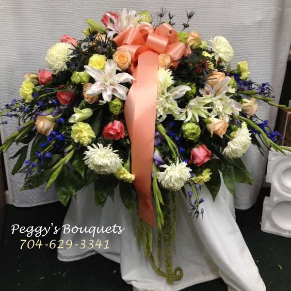 Large floral spray with a peach ribbon and mixed blooms in white, pink, yellow, and blue