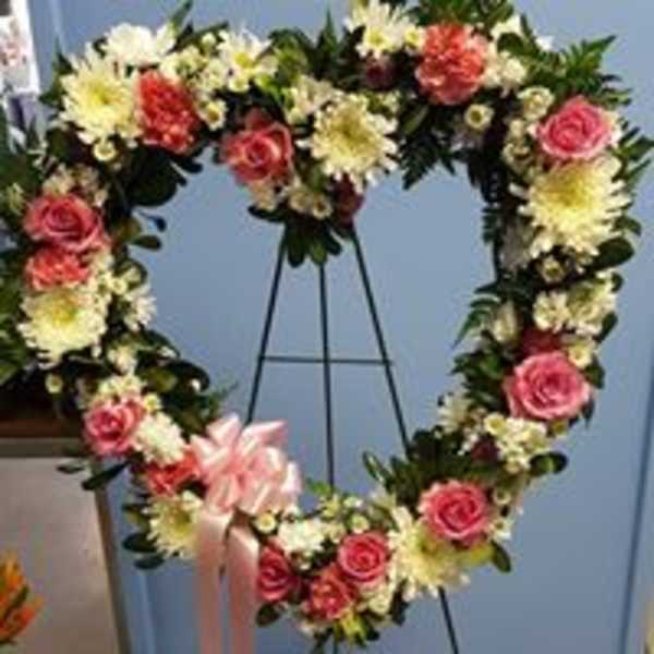 Heart-shaped floral wreath with pink roses and white flowers on a stand