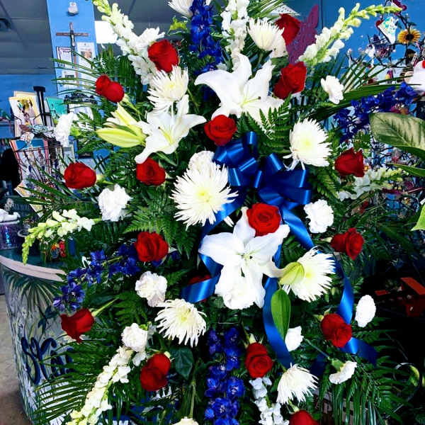 Large standing floral spray with red roses, white lilies, and blue ribbon