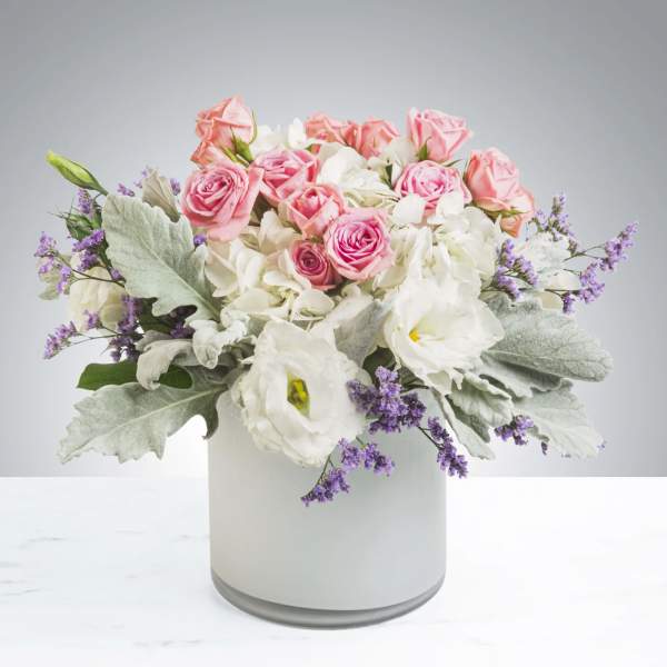 Pink roses and white blooms arranged in a white vase