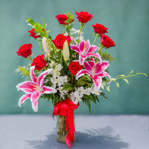 Red roses and pink lilies in a glass vase with a red ribbon