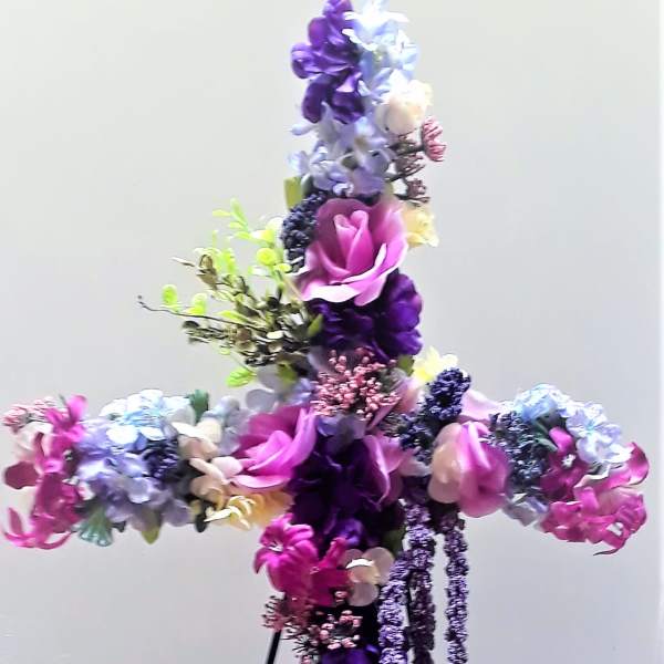 Cross-shaped floral arrangement in purple, pink, and white on a stand
