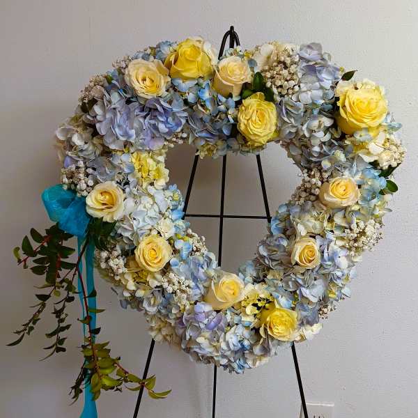Heart-shaped floral wreath with yellow roses and blue hydrangeas on a stand