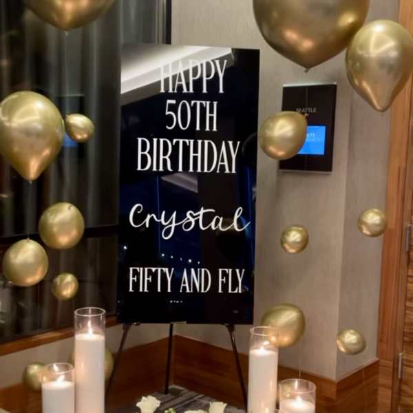 Gold balloons surround a 50th birthday sign with white flowers and candles