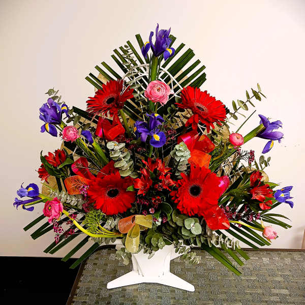 Large floral arrangement with red gerberas, purple irises, and pink blooms in a white vase