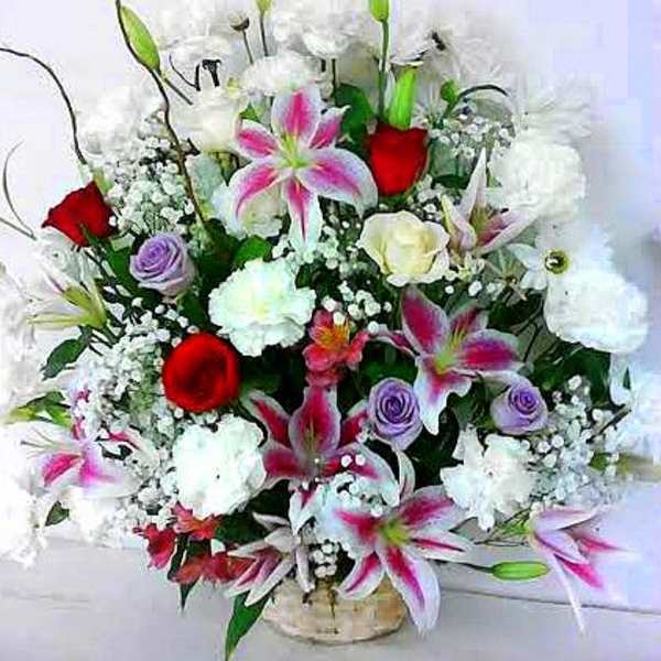 Mixed bouquet of white and pink lilies, red roses, and purple blooms in a vase