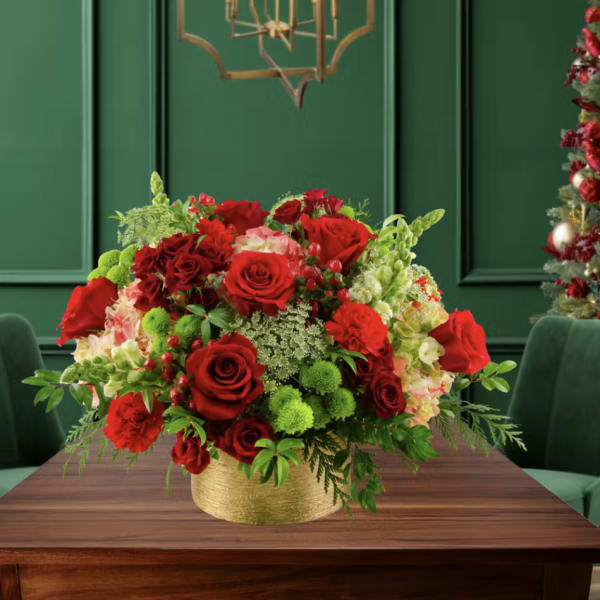 Red roses and mixed flowers arranged in a gold vase on a table