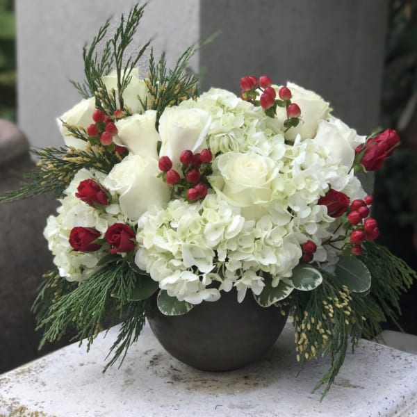 White roses and hydrangeas with red berries in a dark vase