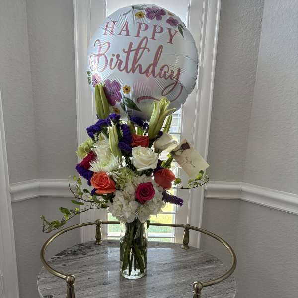 Birthday balloon above a mixed flower arrangement in a glass vase