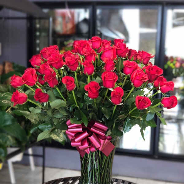 Large bouquet of red roses in a glass vase with a pink ribbon