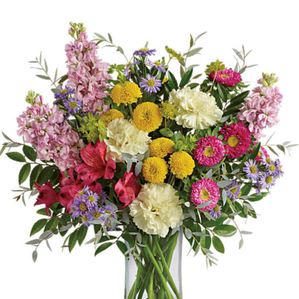Tall mixed bouquet of yellow, pink, purple and white flowers in a clear glass cylinder vase