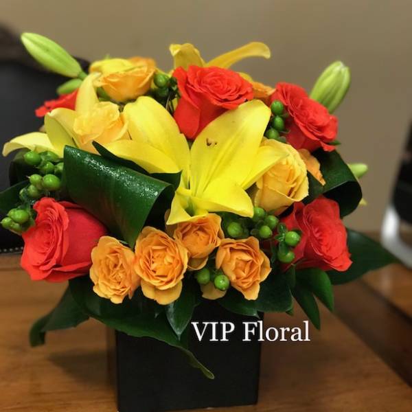 Yellow lilies and red and orange roses in a black vase