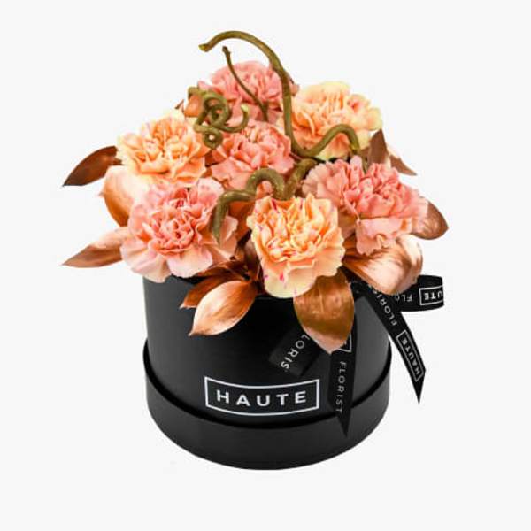 Peach carnations arranged in a black round box with ribbon