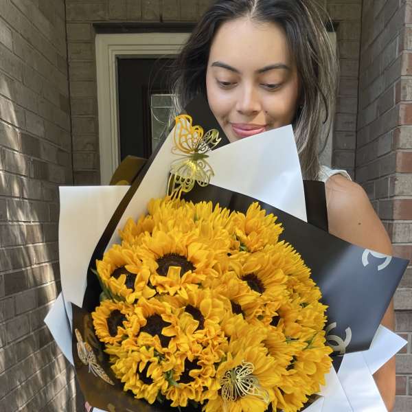 Woman holding a large bouquet of yellow sunflowers wrapped in black and white paper