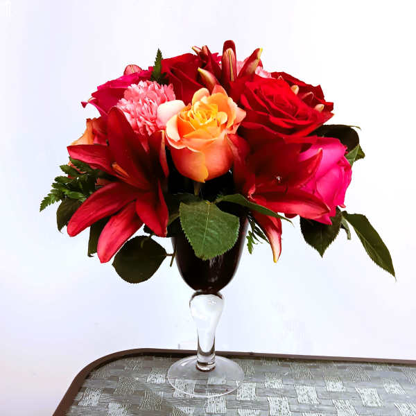 Red and pink flower arrangement in a clear stemmed vase