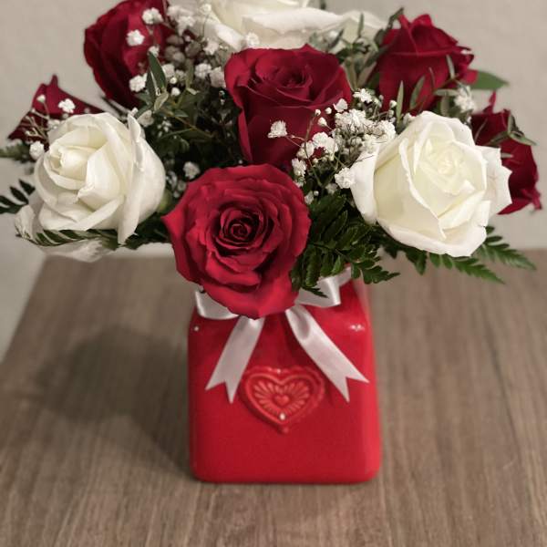 Red and white roses arranged in a red gift box with a white ribbon