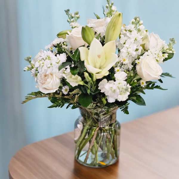 White floral bouquet in a clear glass vase on a wooden table