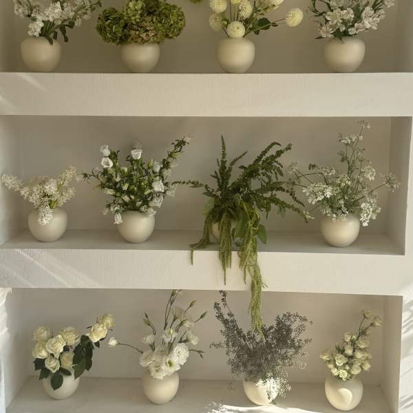 Shelved display of small white floral arrangements in cream vases