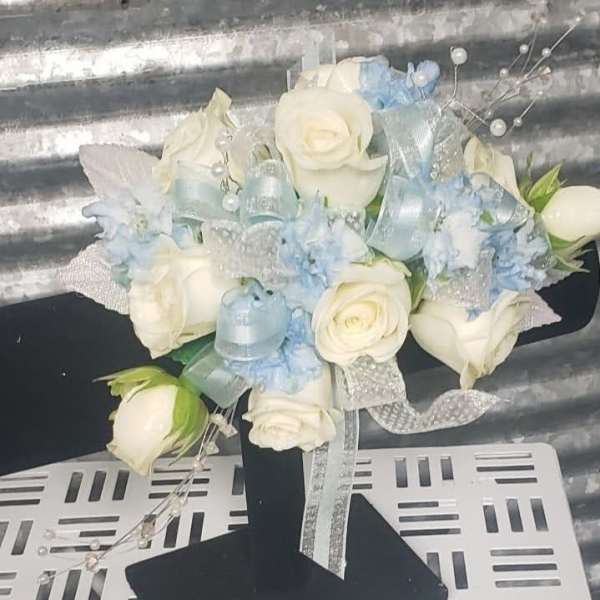 White roses and pale blue flowers arranged with ribbons on a black stand