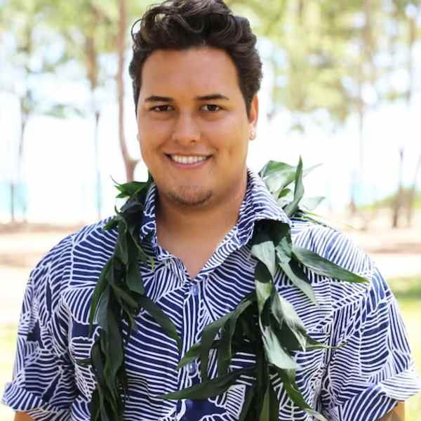Man wearing a leafy lei and patterned shirt outdoors