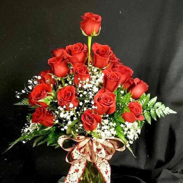 Red roses arranged in a glass vase with baby's breath and a ribbon bow