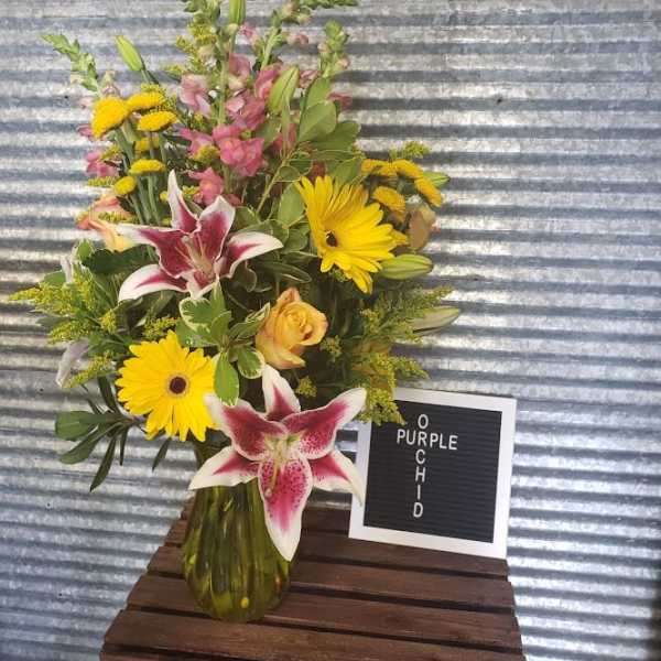 Mixed bouquet with yellow daisies, pink lilies, and roses in a glass vase