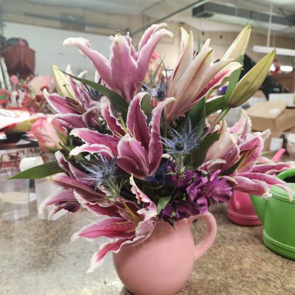 Pink and white lilies arranged in a pink pitcher vase