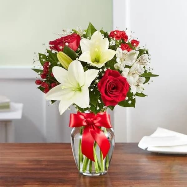 Bouquet of red roses and white lilies in a glass vase with a red ribbon