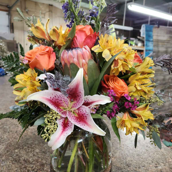 Mixed bouquet with pink lily, orange roses, and yellow alstroemeria in a glass vase