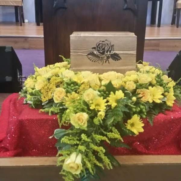 Yellow floral arrangement around a wooden urn with a rose emblem
