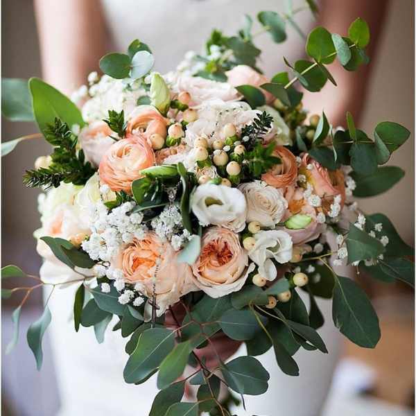 Bride holding a bouquet of peach and white flowers with greenery