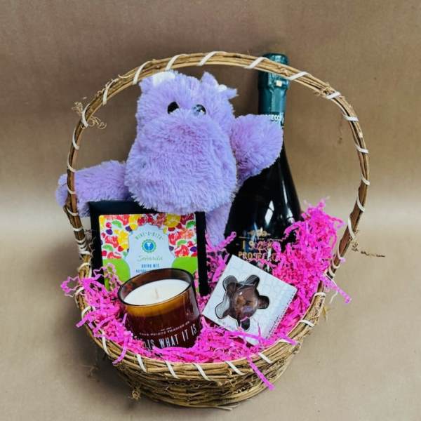Gift basket with a plush purple hippo, candle, chocolate, and a bottle