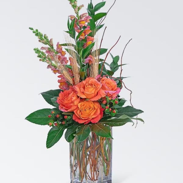 Orange roses in a clear glass vase with tall pink blooms