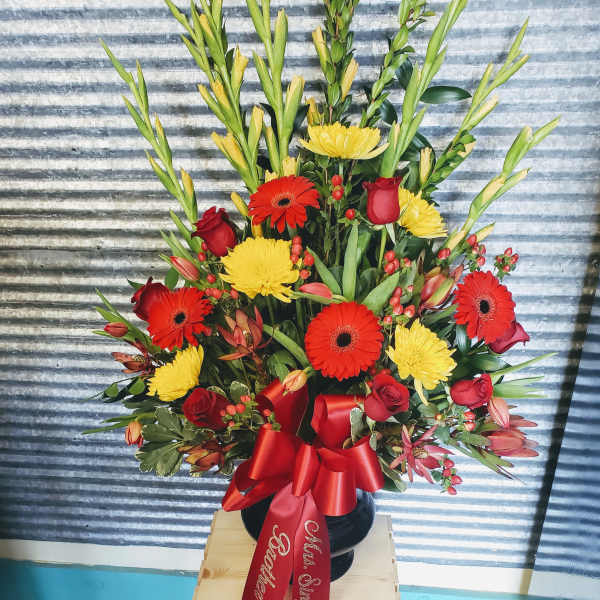 Tall floral arrangement with red roses, gerbera daisies, and yellow blooms in a black vase
