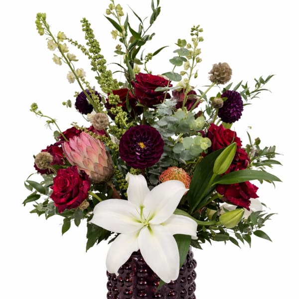 Mixed bouquet with red roses, white lily, and purple blooms in a dark vase