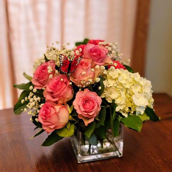 Pink roses and white hydrangeas in a square glass vase with a butterfly accent