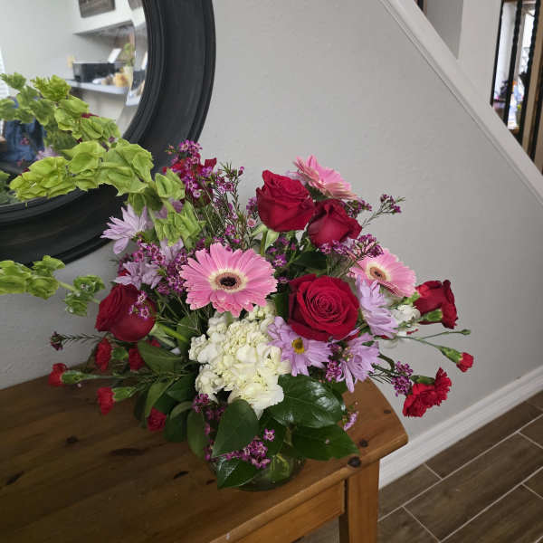 Mixed bouquet of red roses, pink gerberas, and white hydrangea in a glass vase