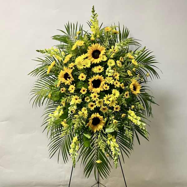 Standing floral spray with yellow sunflowers and daisies on a black easel