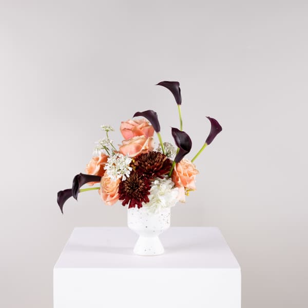 Peach roses and dark calla lilies in a white vase