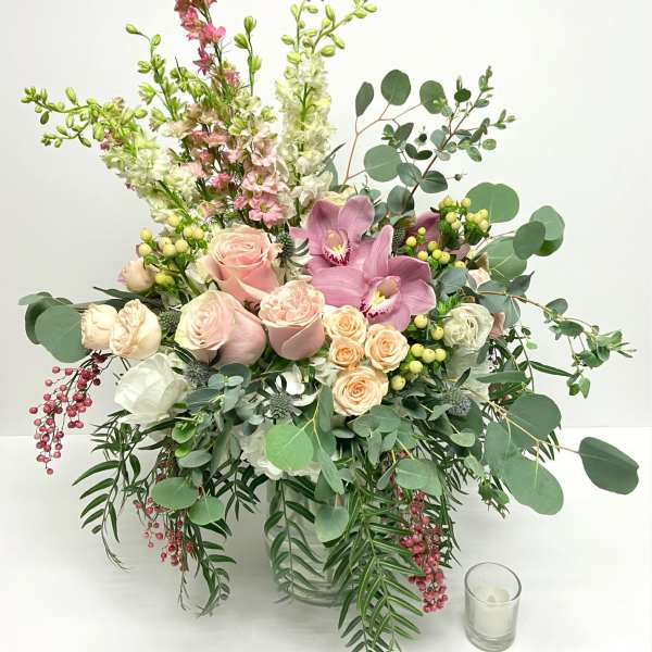 Large pastel bouquet in a clear glass vase with pink roses and orchids
