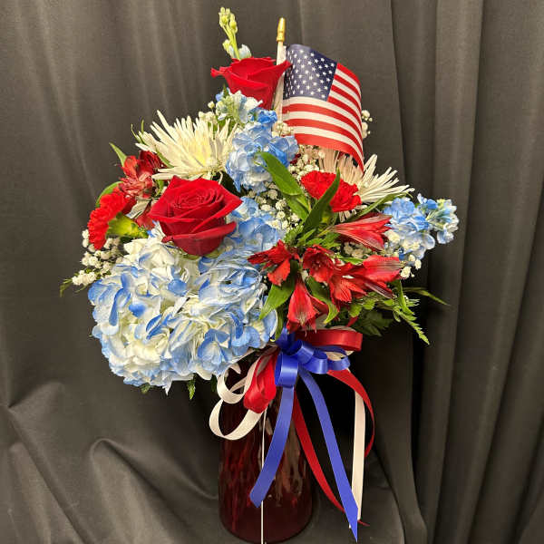 Red, white, and blue floral arrangement in a vase with an American flag