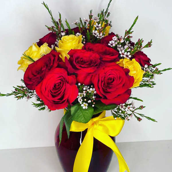 Red and yellow roses in a dark vase with a yellow ribbon